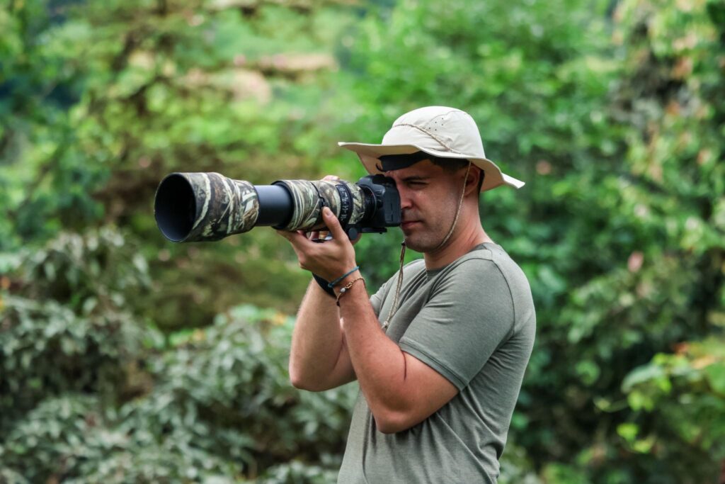 Wildlife adventure photographer capturing nature with a telephoto lens in a green forest