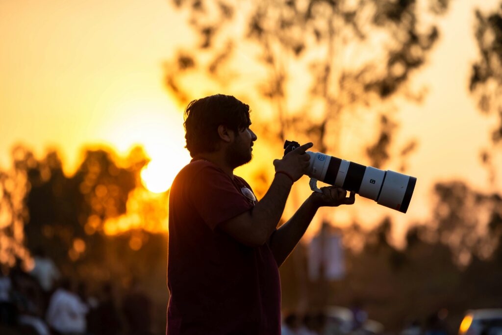 Silhouette of a photographer with a telephoto lens capturing the sunset outdoors.
